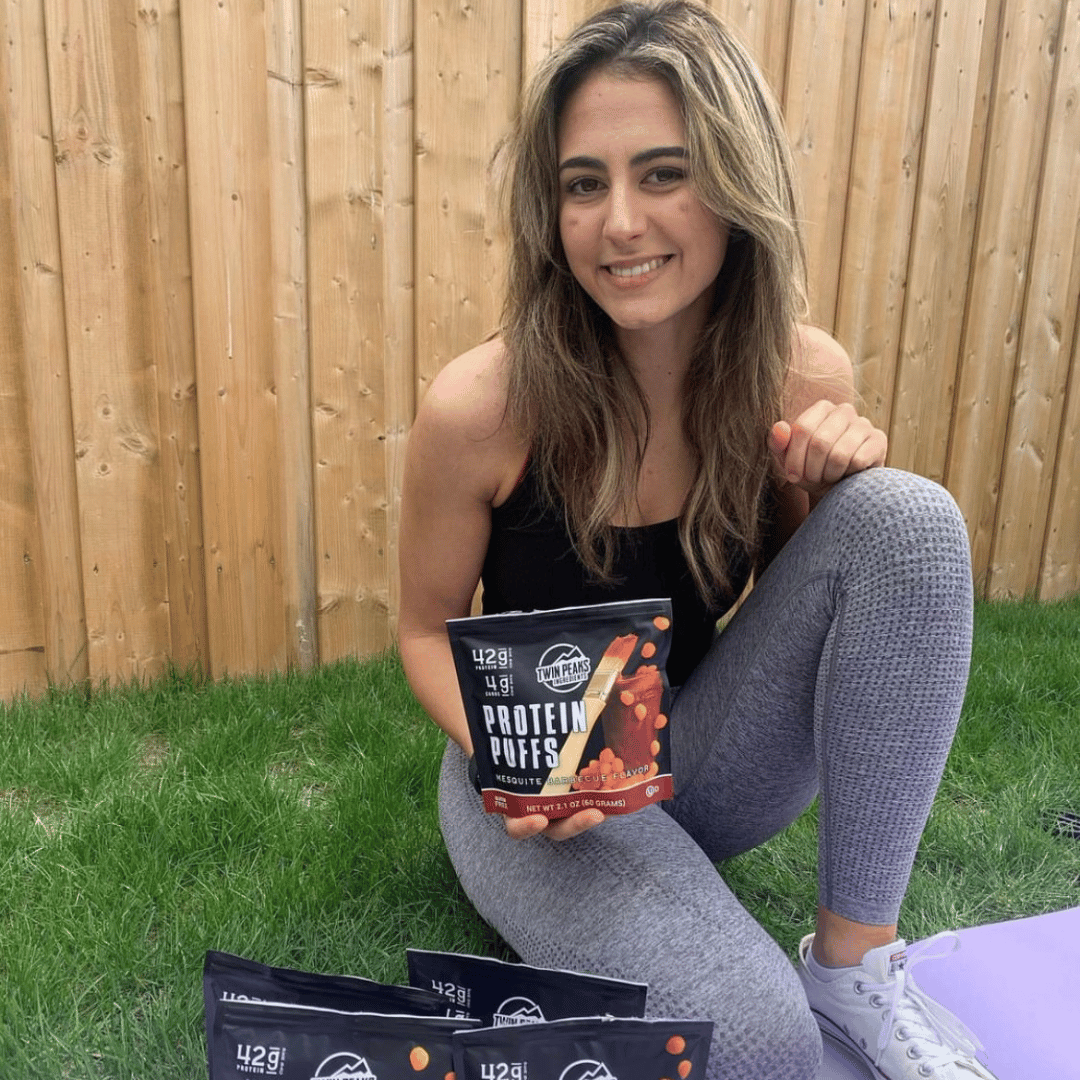 Girl Wearing Workout Apparel Holding a Mesquite BBQ Protein Puff Bag